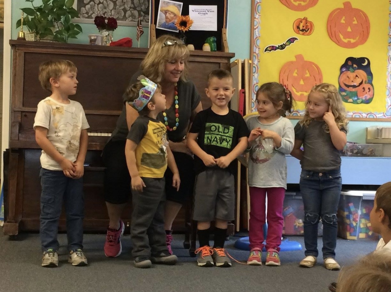 Children singing together in front of a piano and pumpkin decorations