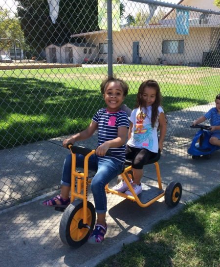 Two girls riding a tandem tricycle outdoors