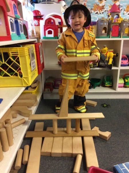 Boy dressed as a firefighter building with wooden blocks