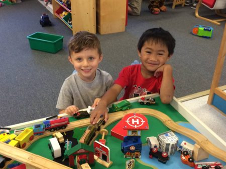 Two boys playing at a wooden train table