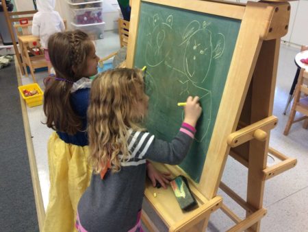 Two girls drawing on a chalkboard easel