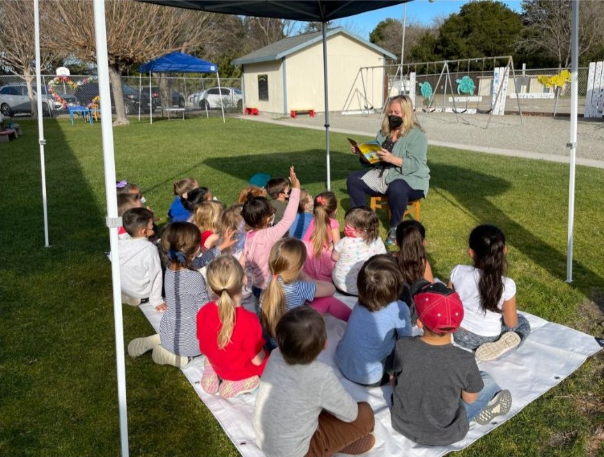 Children sitting outdoors under a canopy for story time